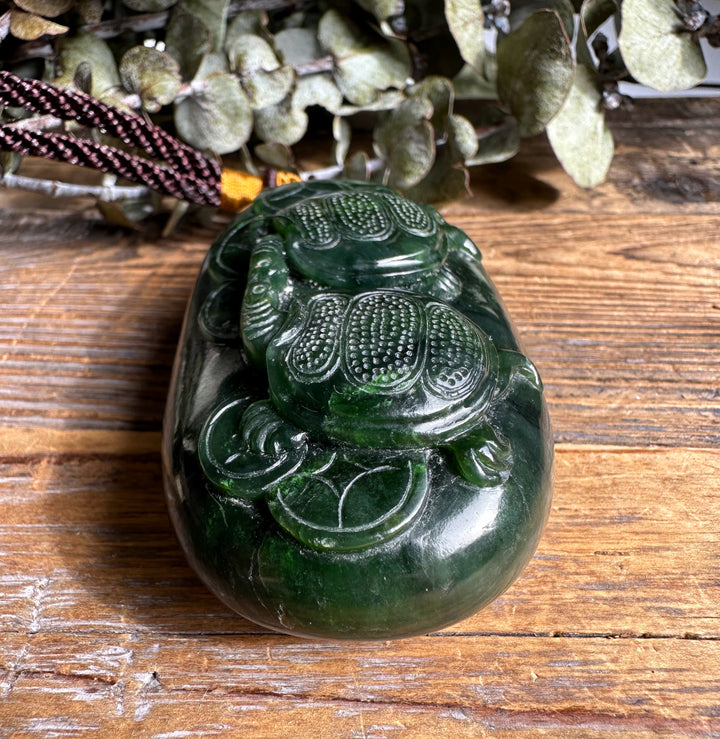 Glossy dark green Canadian jade pendant carved with two turtles on a cord.