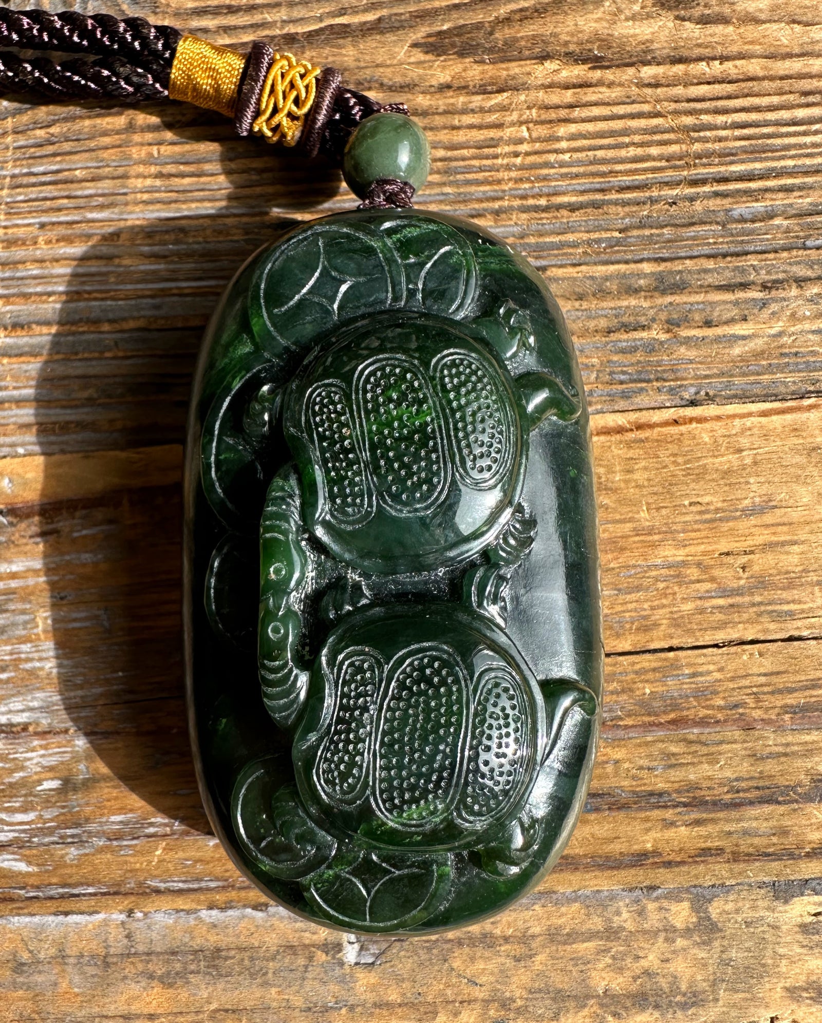 Two turtle carved green jade hand held pendant on a brown cord with a small round bead above