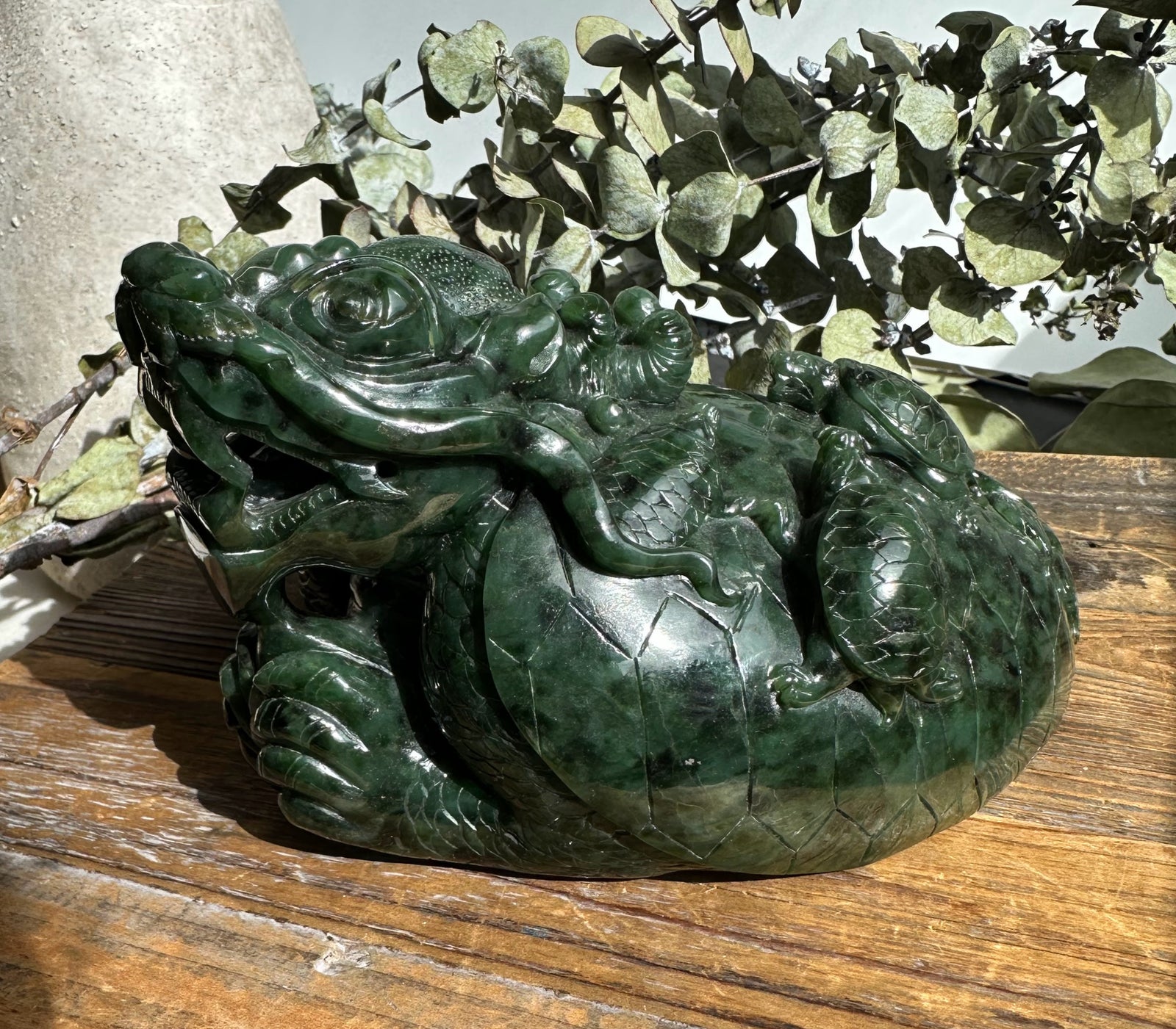 Dark green jade dragon turtle carving with a dragon atop the turtle's shell on a wooden surface