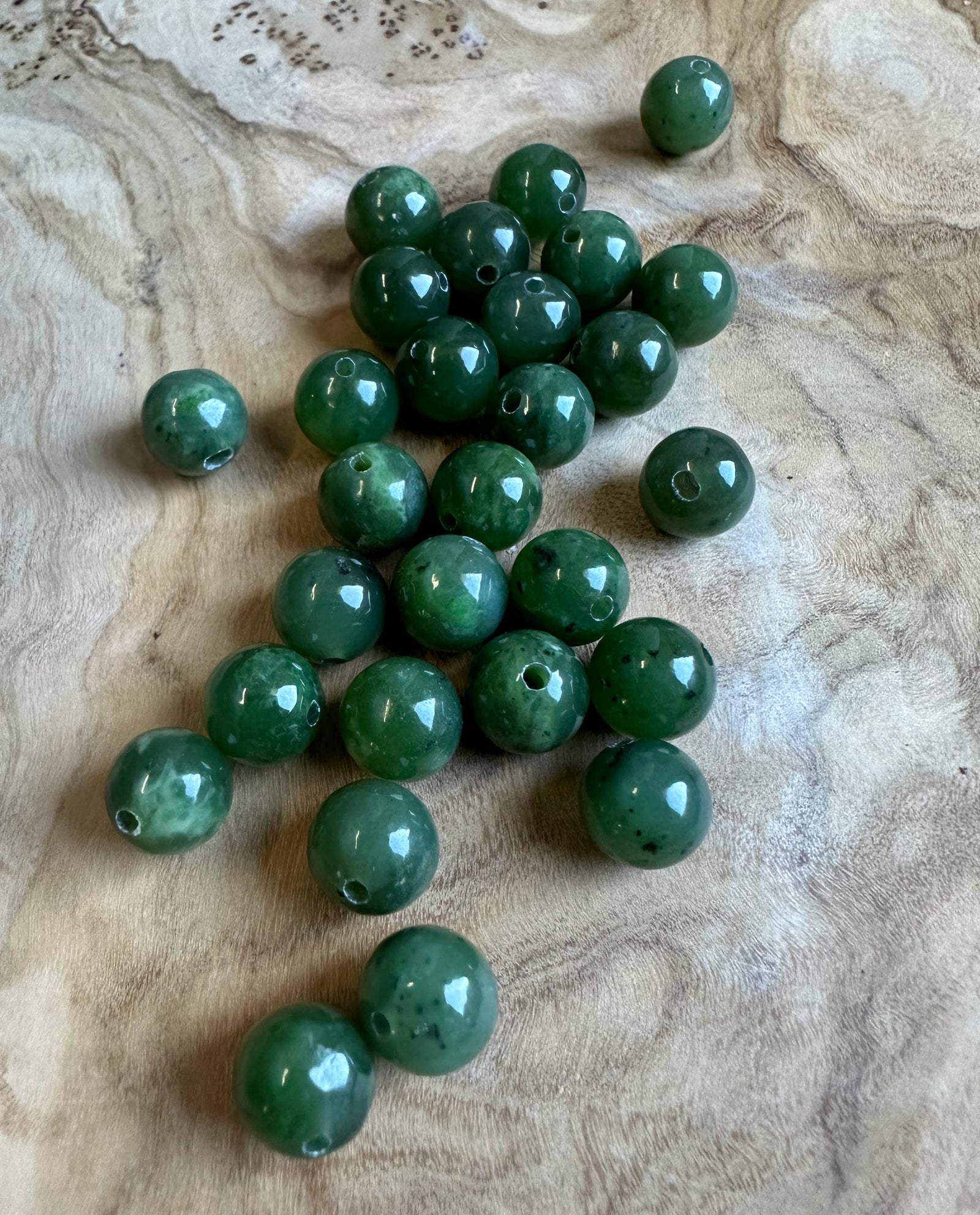 Cluster of 8mm Canadian jade beads with drilled holes on a textured beige surface