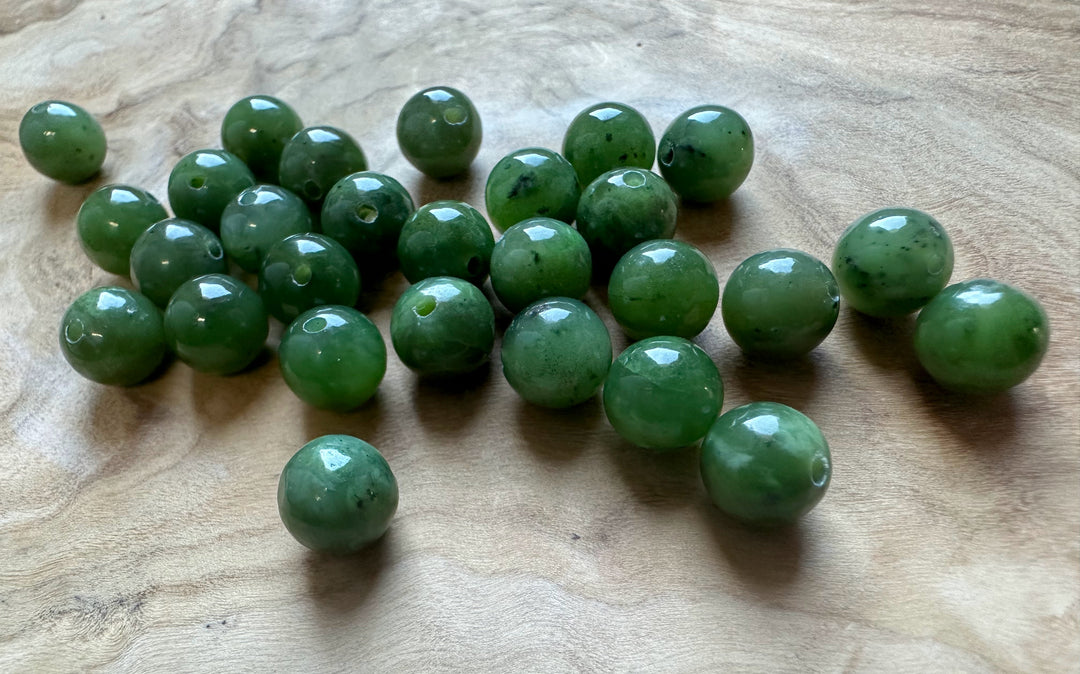 Group of 8mm Canadian Jade beads with regular holes spread on a wooden surface