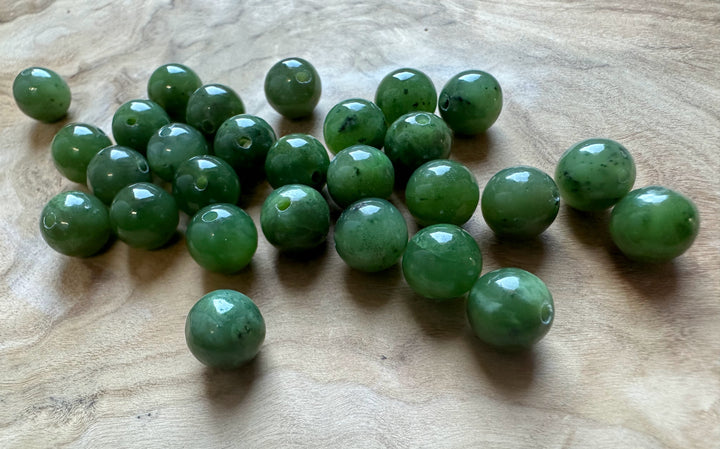 Group of 8mm Canadian Jade beads with regular holes spread on a wooden surface
