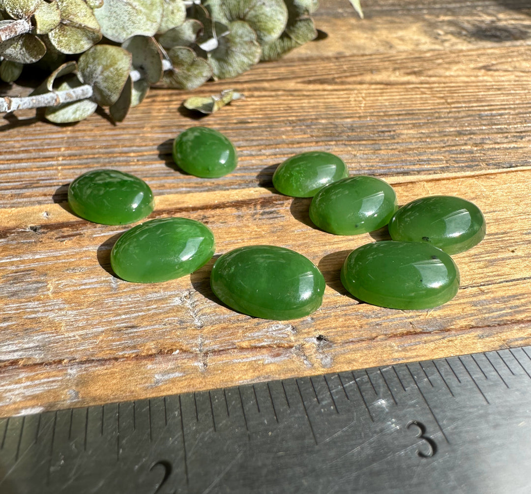 Dusty sage leaves with several green oval cabochons scattered on a weathered wooden surface