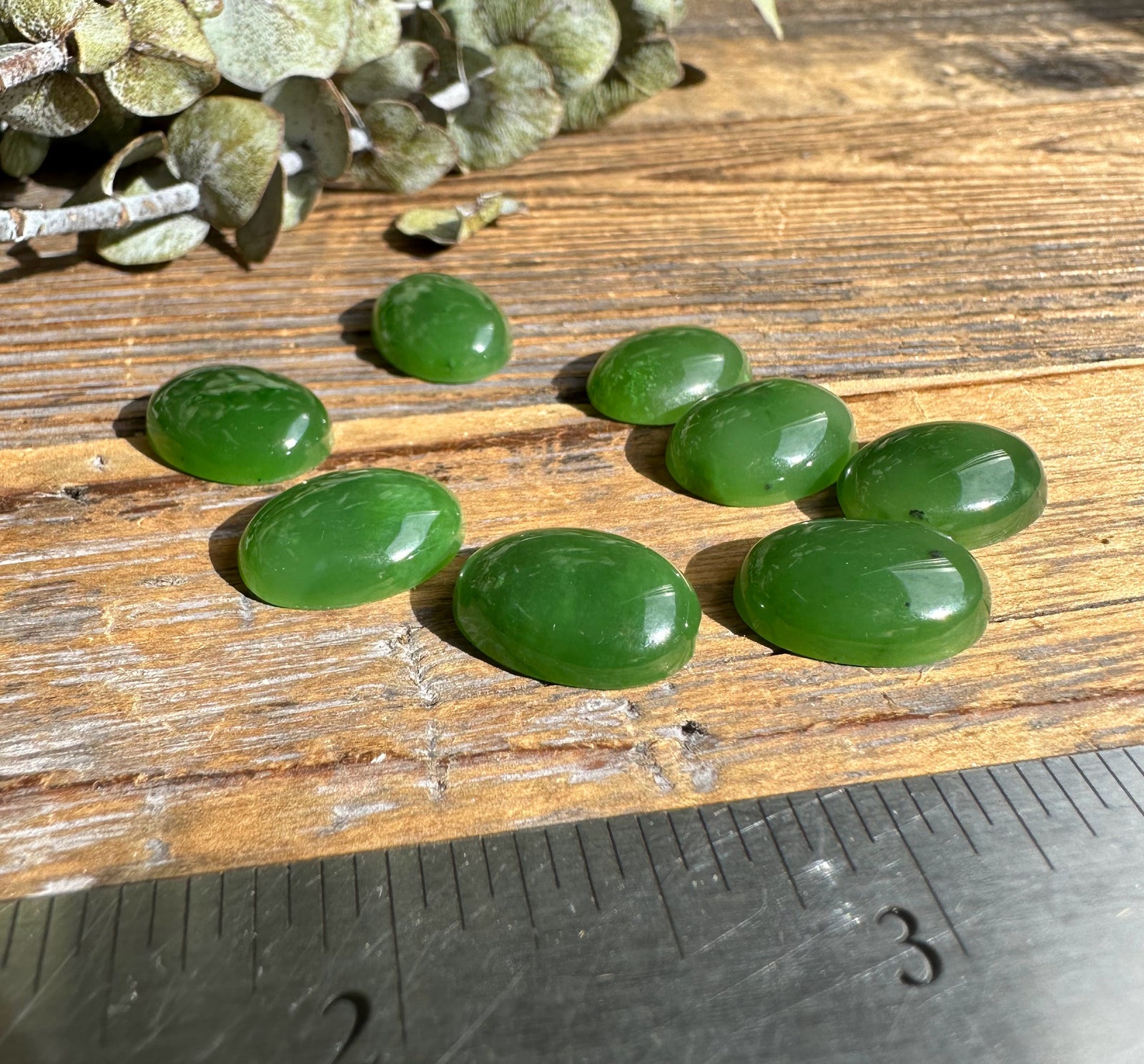 Dusty sage leaves with several green oval cabochons scattered on a weathered wooden surface