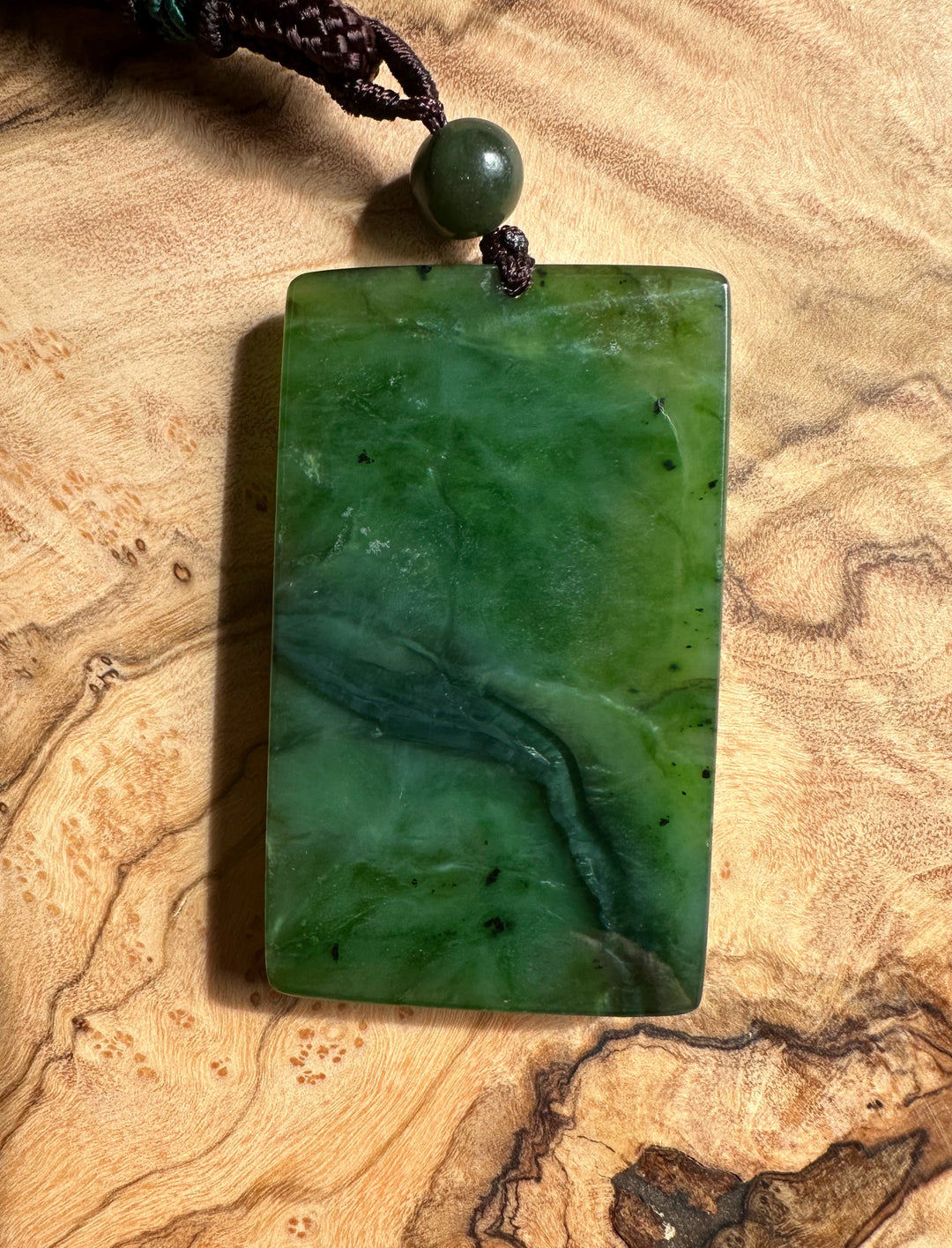 Rectangular dark green jade pendant with a round bead on a dark braided cord