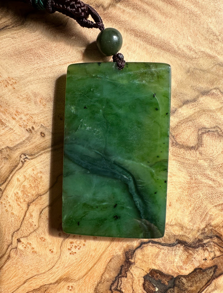 Rectangular dark green jade pendant with a round bead on a dark braided cord