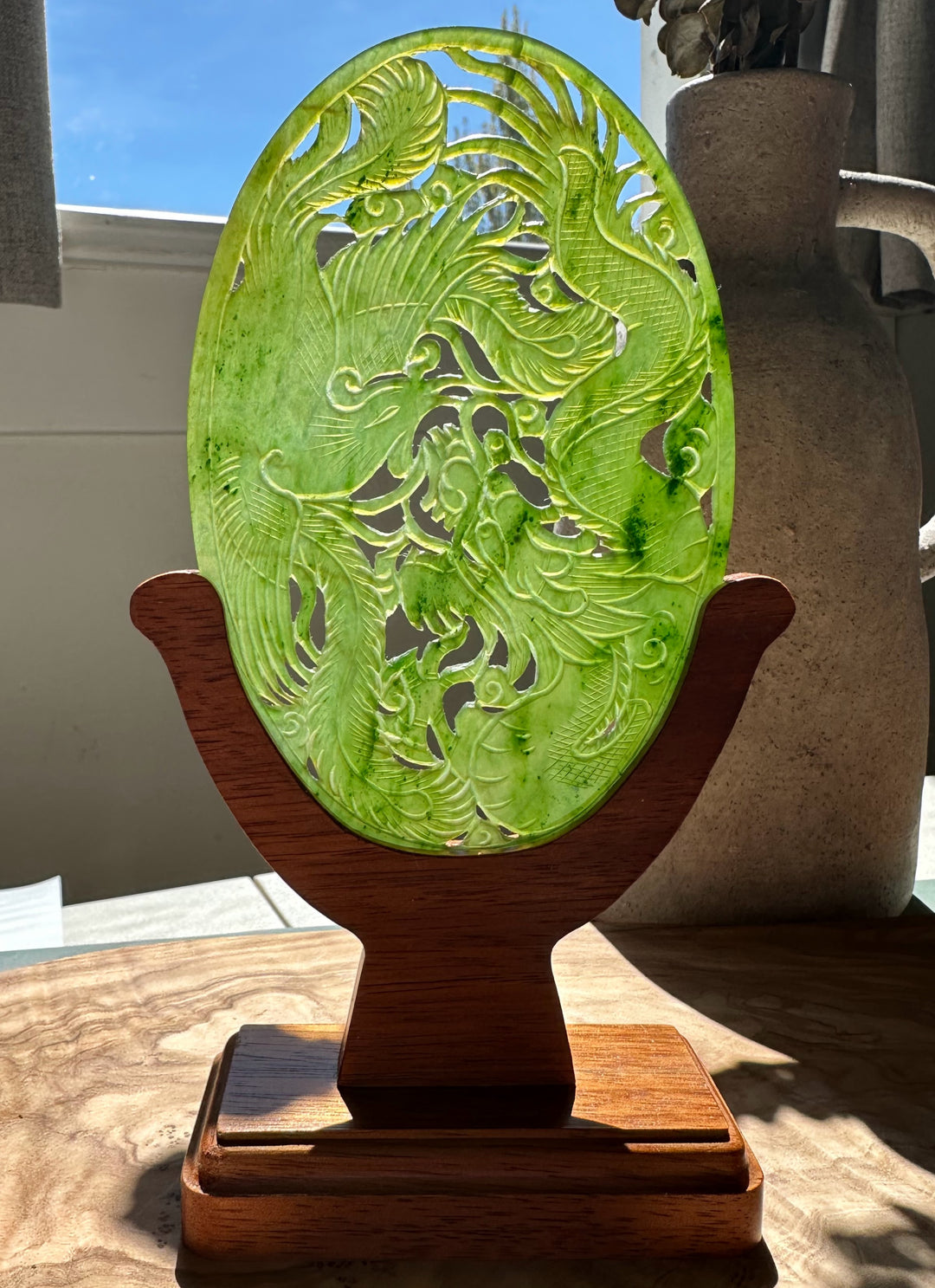 Bright green jade oval screen featuring dragons and phoenixes on a wooden stand