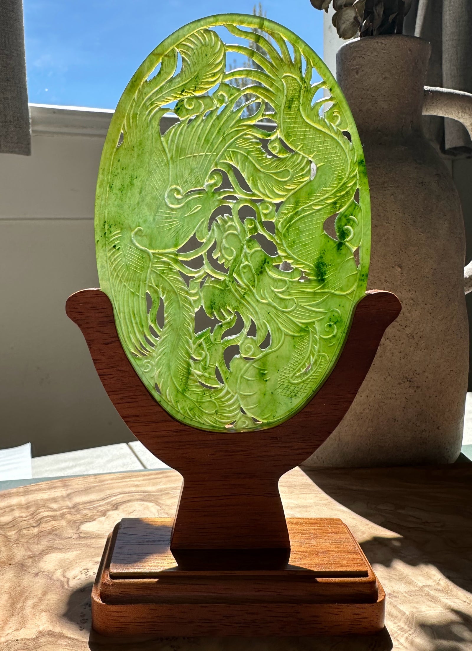 Bright green jade oval screen featuring dragons and phoenixes on a wooden stand