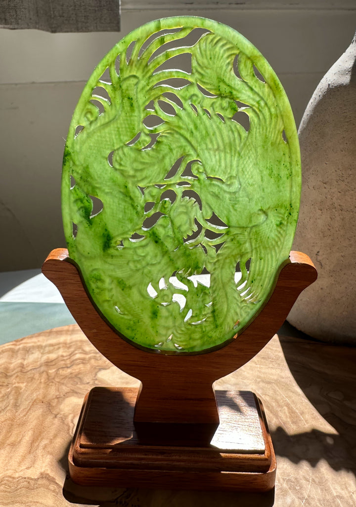 Vivid lime green jade oval screen with a dragon and phoenix carving on a wooden display stand