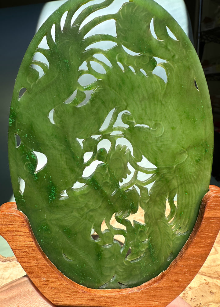 Green jade oval screen carved with dragon and phoenix silhouettes on a wooden display stand