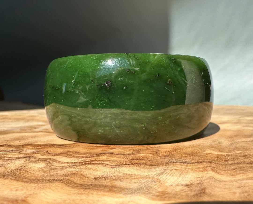Wide Cassiar Jade Bangle in green and tan tones resting on a wood surface