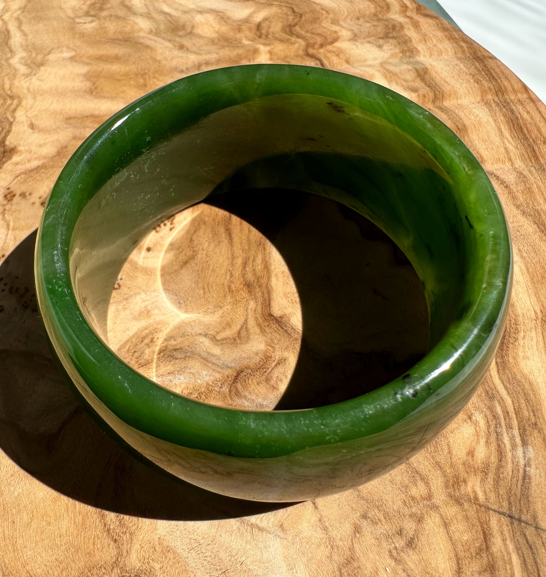 Top view of Wide Cassiar Jade Bangle showing green rim and inner hollow space on wood