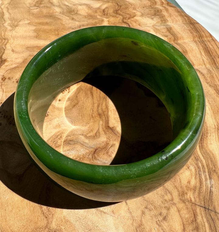 Top view of Wide Cassiar Jade Bangle showing green rim and inner hollow space on wood