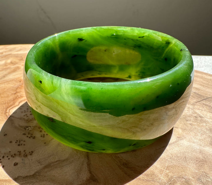 Wide Cassiar Jade Bangle in bright green with cream banding on a wooden surface