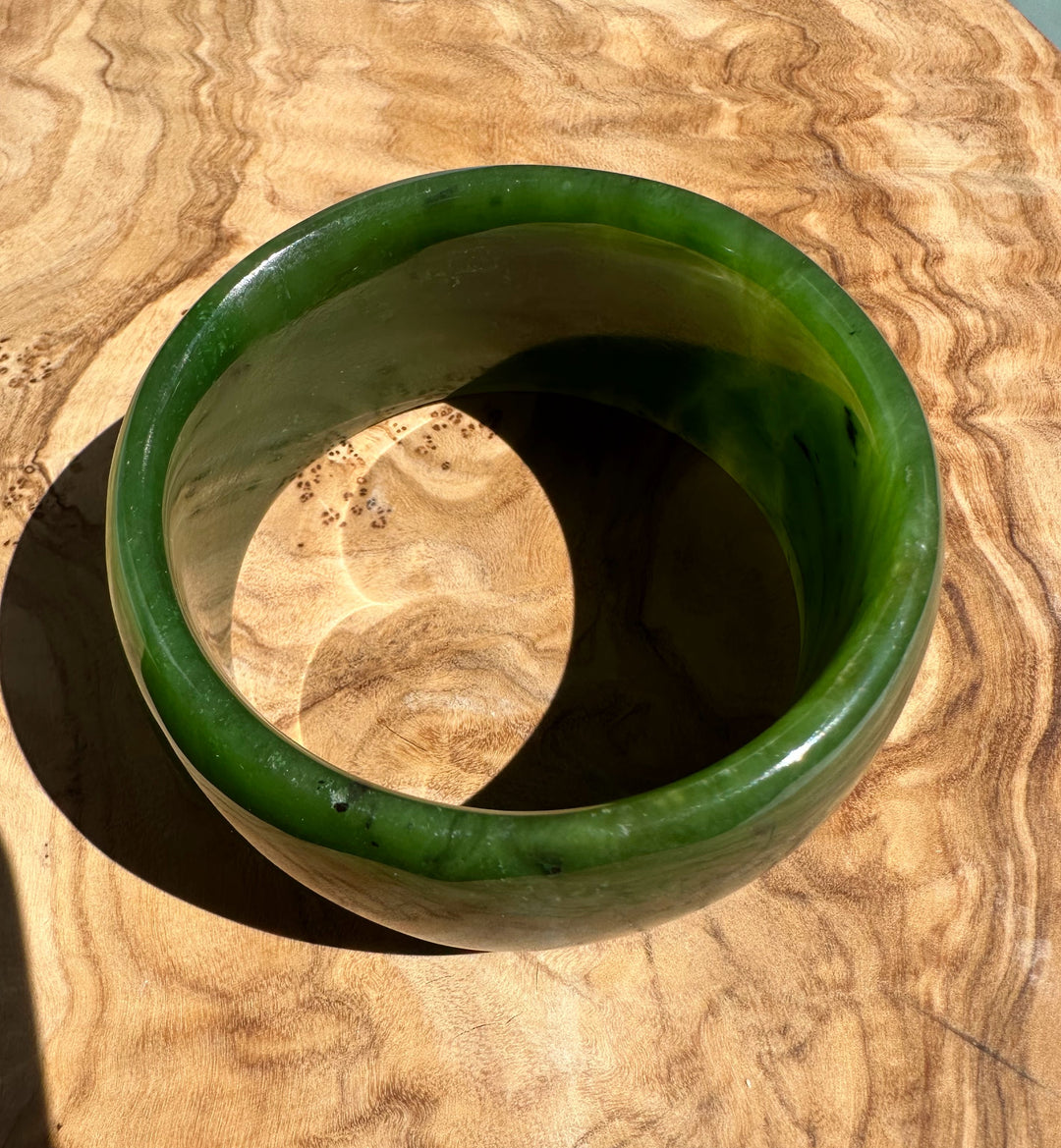 Top view of the wide jade bangle showing green hues and lighter bands on a wooden table