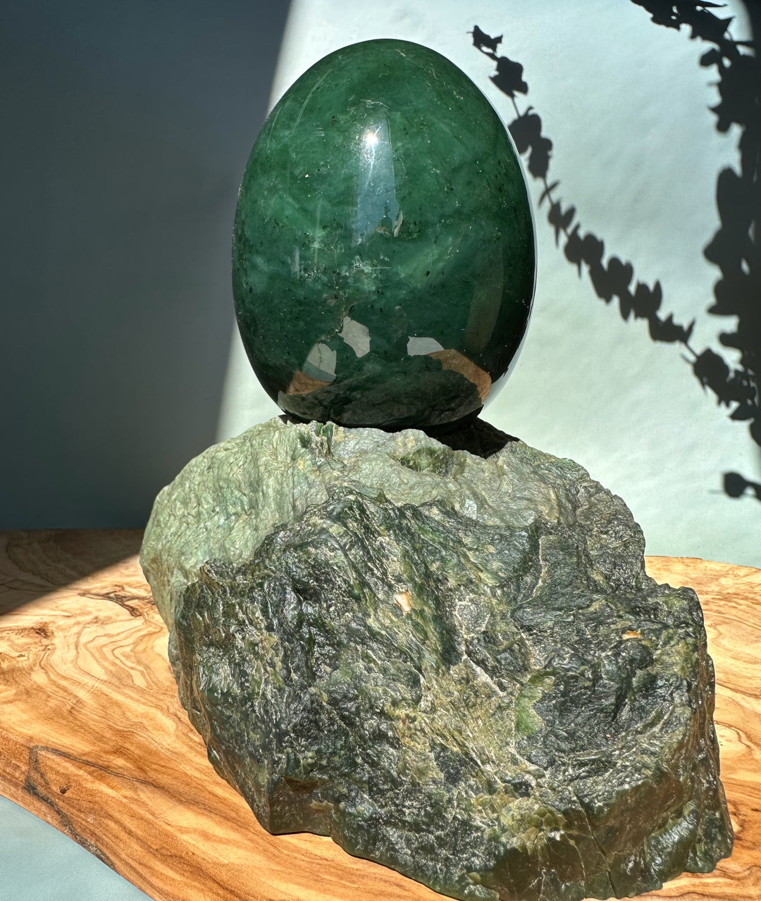Large green jade egg on a rough rock base set on a wooden surface