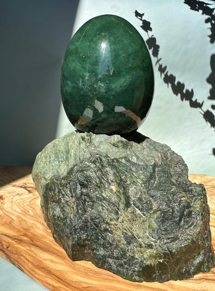 Green jade egg balanced on a jagged rock base under strong sunlight.