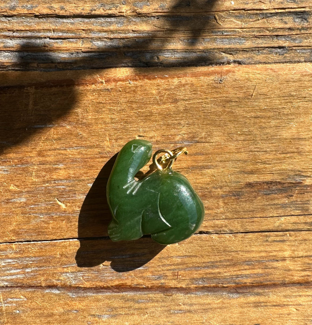 Green dinosaur pendant with a gold loop on a wooden surface