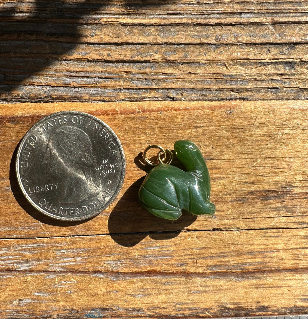 Green dinosaur charm with a small gold loop beside a US quarter for scale