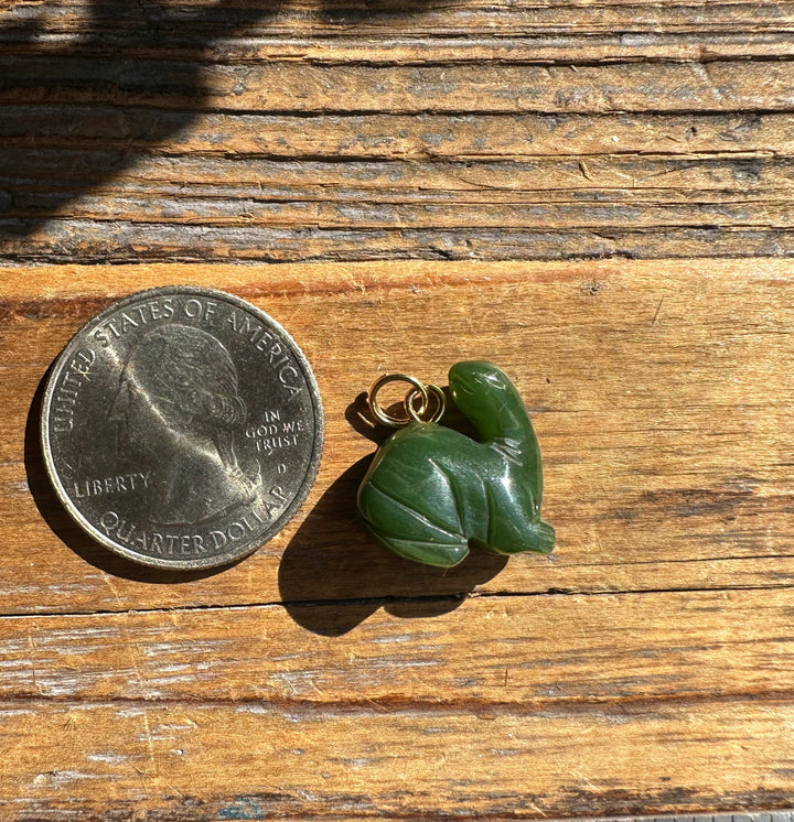 Green dinosaur charm with a small gold loop beside a US quarter for scale