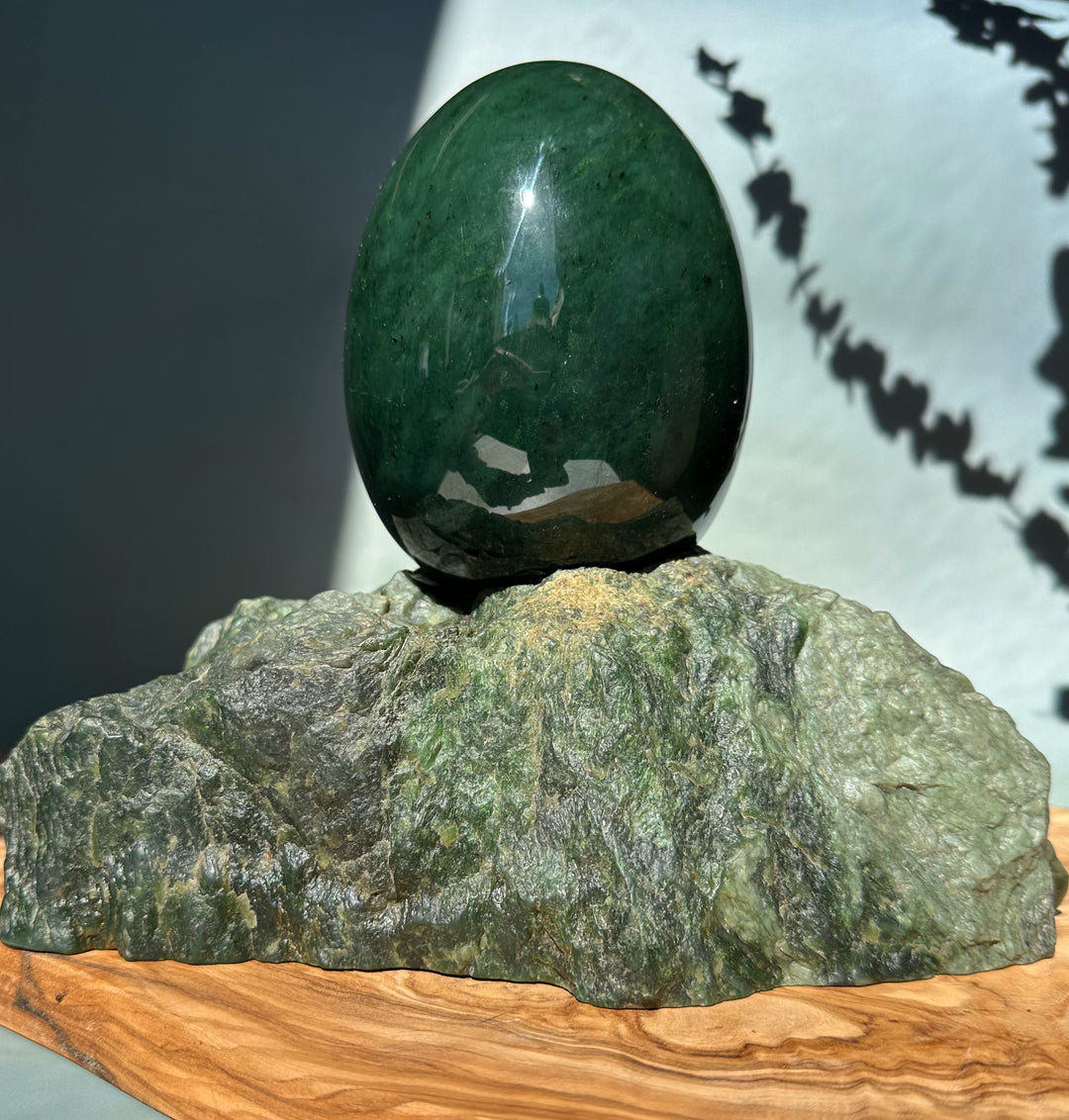 Large polished jade egg balanced on a textured green rock base on a wooden platform
