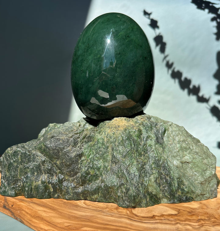 Large polished jade egg balanced on a textured green rock base on a wooden platform