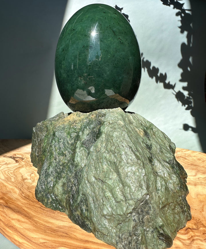 Large green jade egg perched on a rough rock base on a wooden surface.