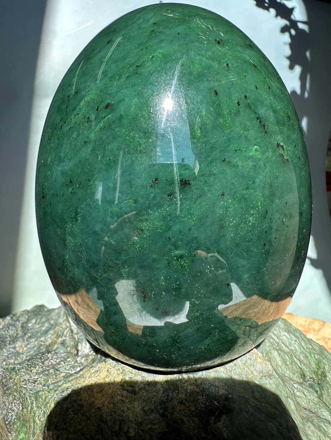Polished green jade egg resting on a rough rock base with bright light reflection.