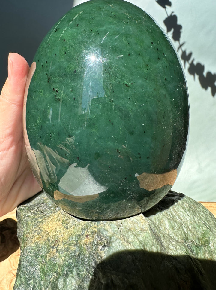 Close up of a polished green jade egg held by hand atop a textured rock base for scale.