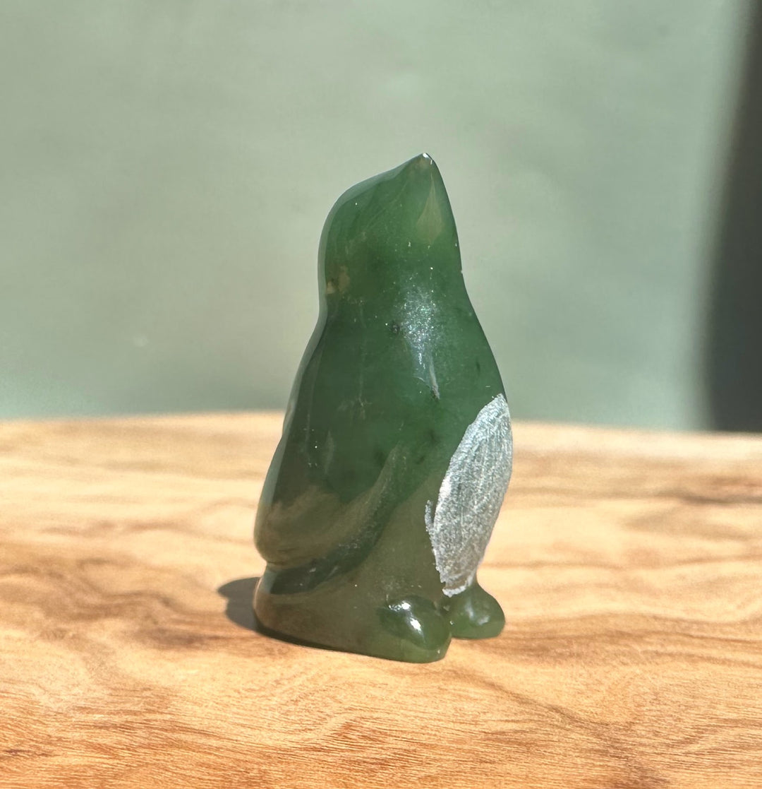 Back view of a green Canadian Jade Penguin figurine on a wooden surface