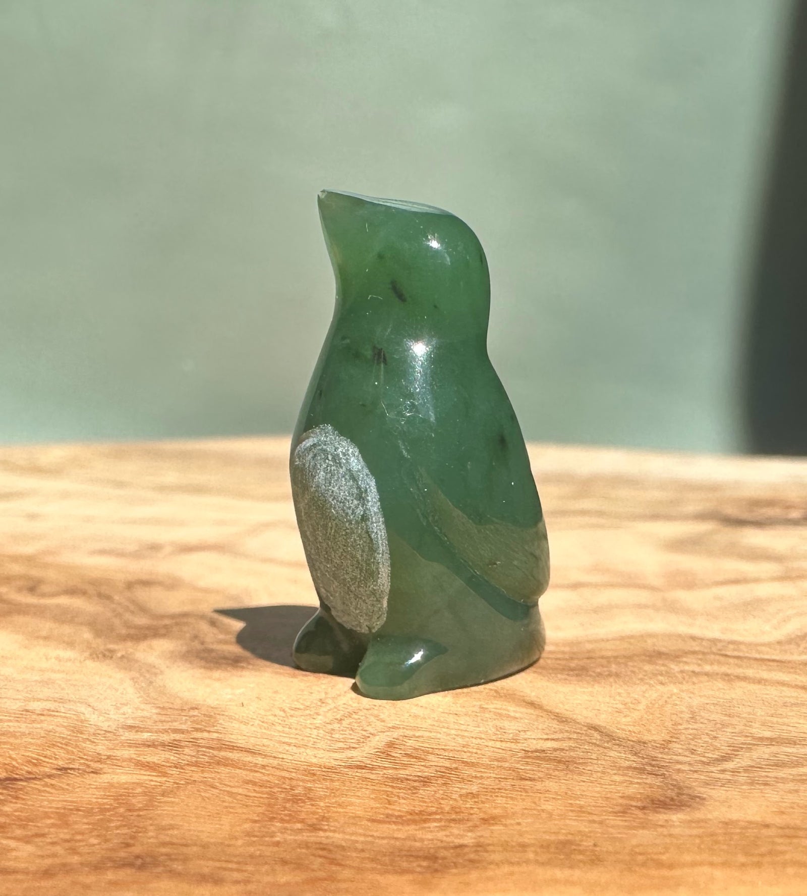 Canadian Jade Penguin figurine in deep green with a silver patch on its side on a wooden surface
