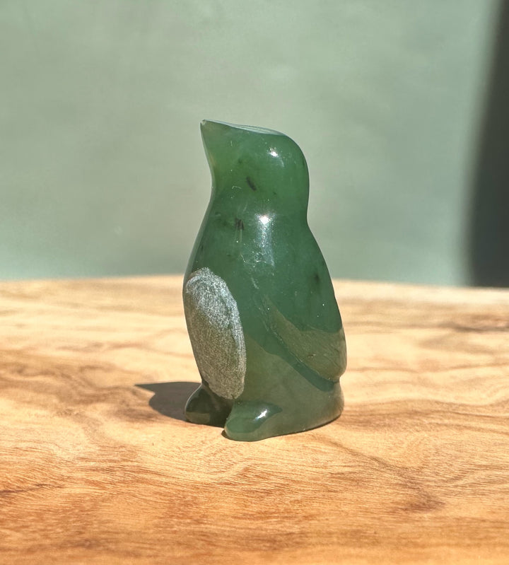 Canadian Jade Penguin figurine in deep green with a silver patch on its side on a wooden surface