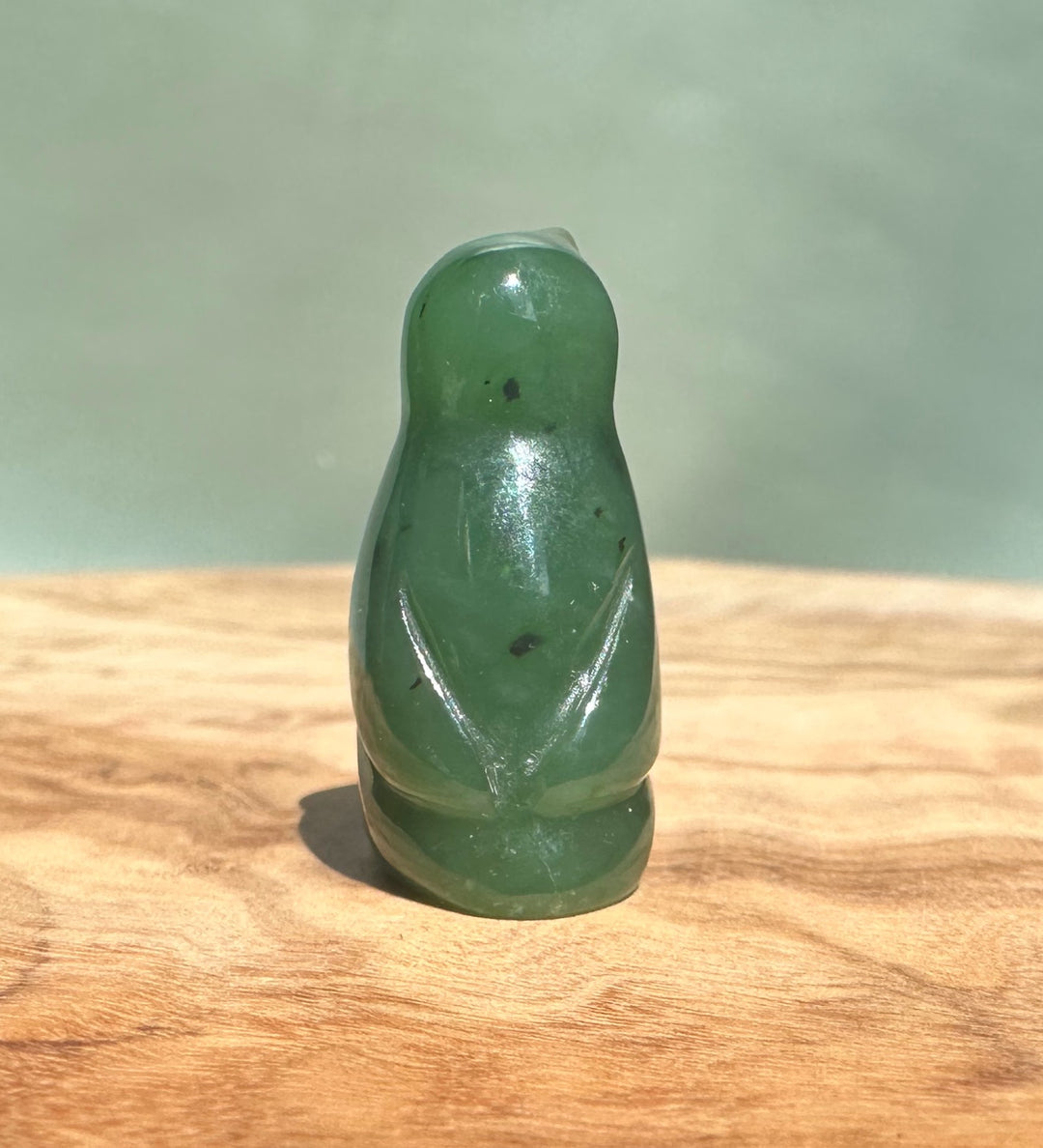Small Canadian jade penguin figurine about 1 inch tall on a wooden surface