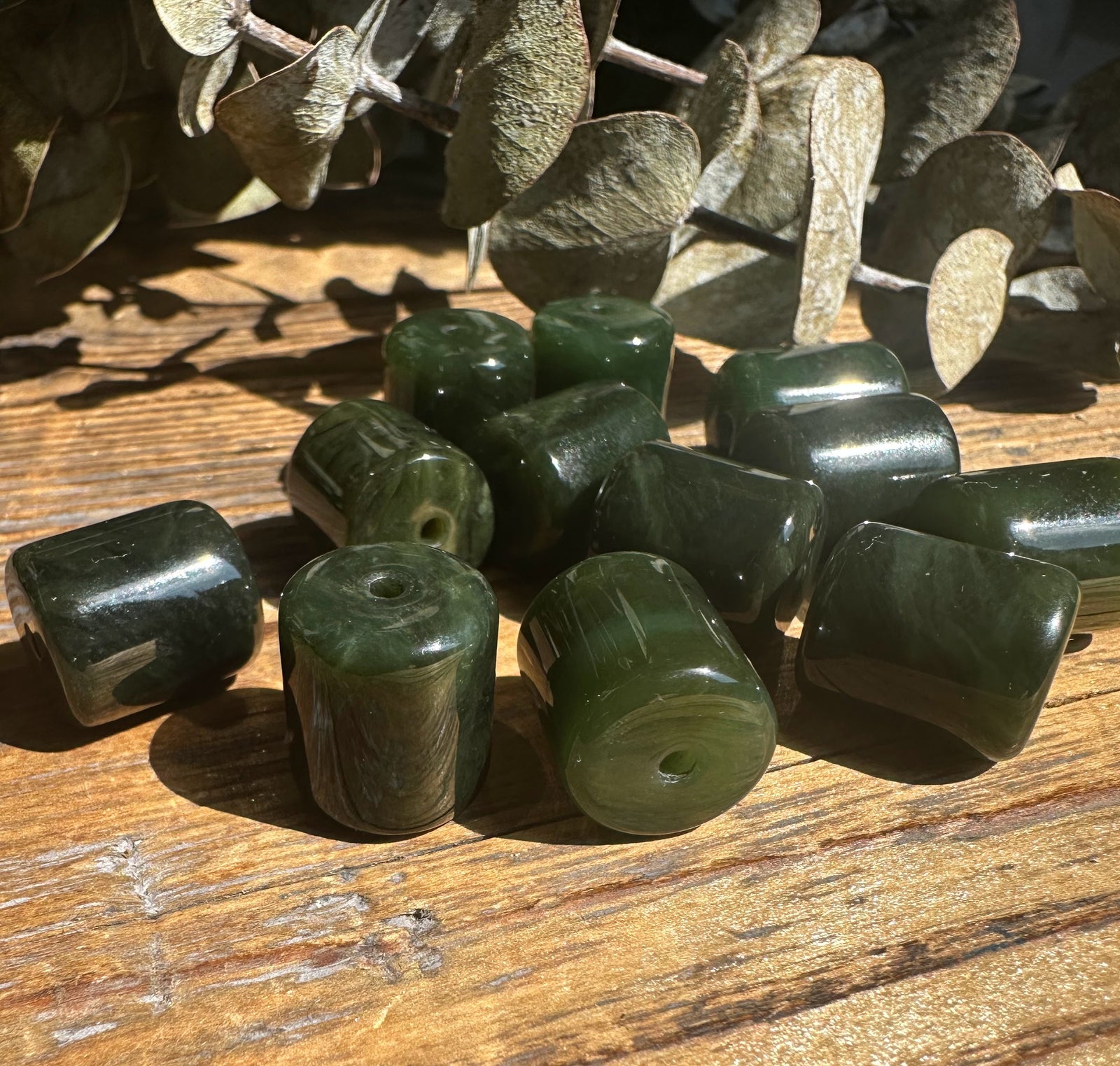 Group of dark green jade barrel beads with central holes scattered on a wooden surface