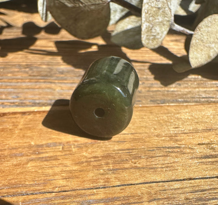 Dark green jade barrel bead 13x15mm with a hole on a wood surface
