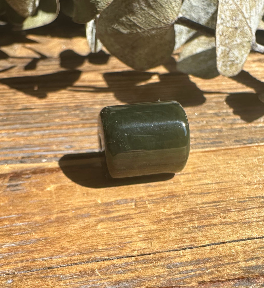 Green jade barrel bead 13x15mm with a hole shown on wood surface