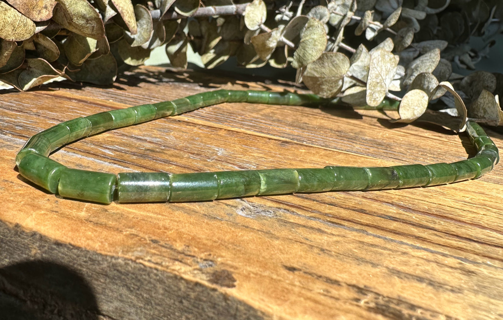 Green Siberian Jade tube bead necklace resting on a rustic wooden surface.