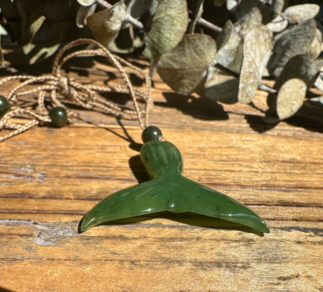Close up of jade whale tail pendant on a brown cord with metal loop details