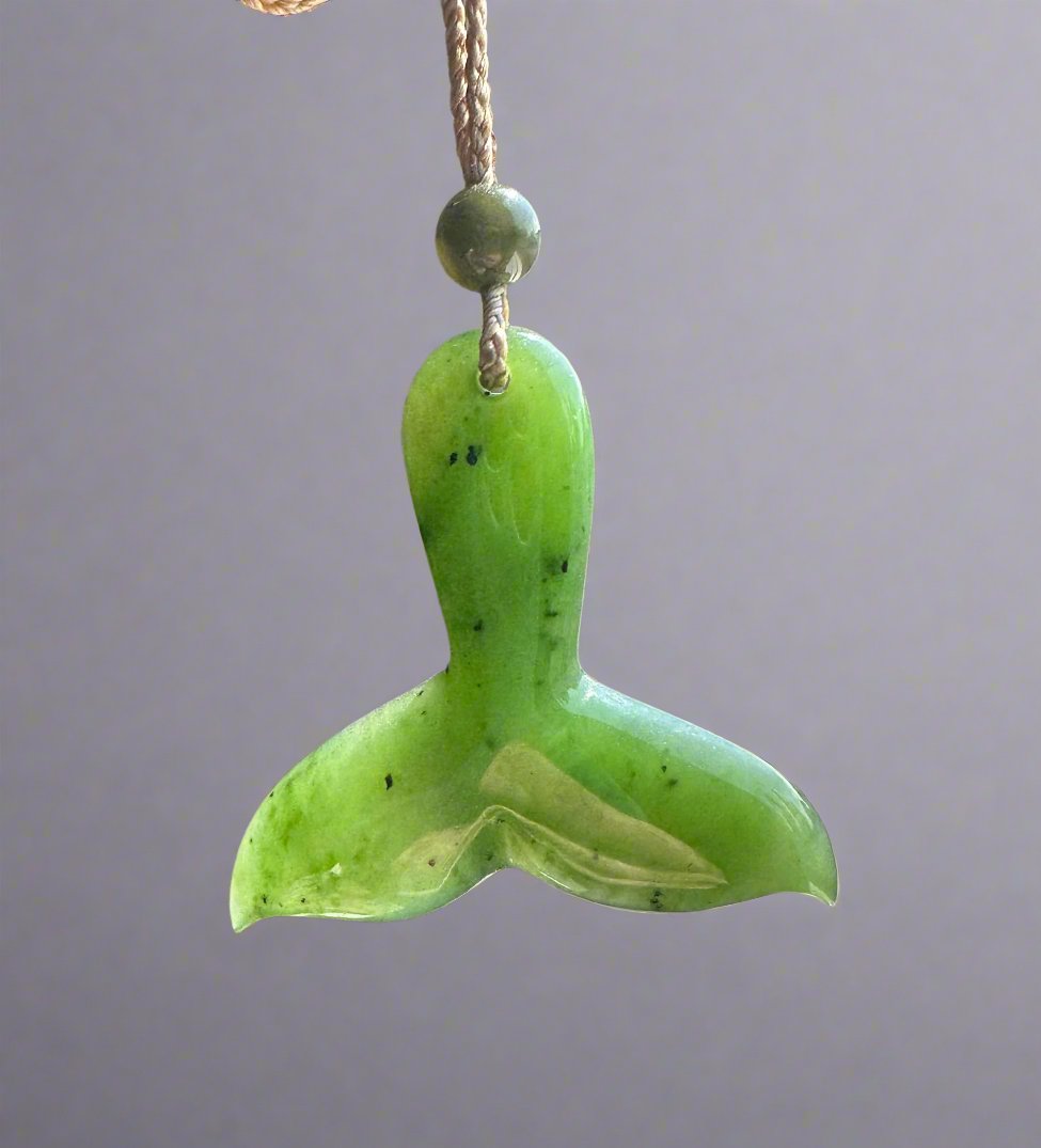 Bright green jade whale tail pendant with a round bead above on a natural fiber cord.
