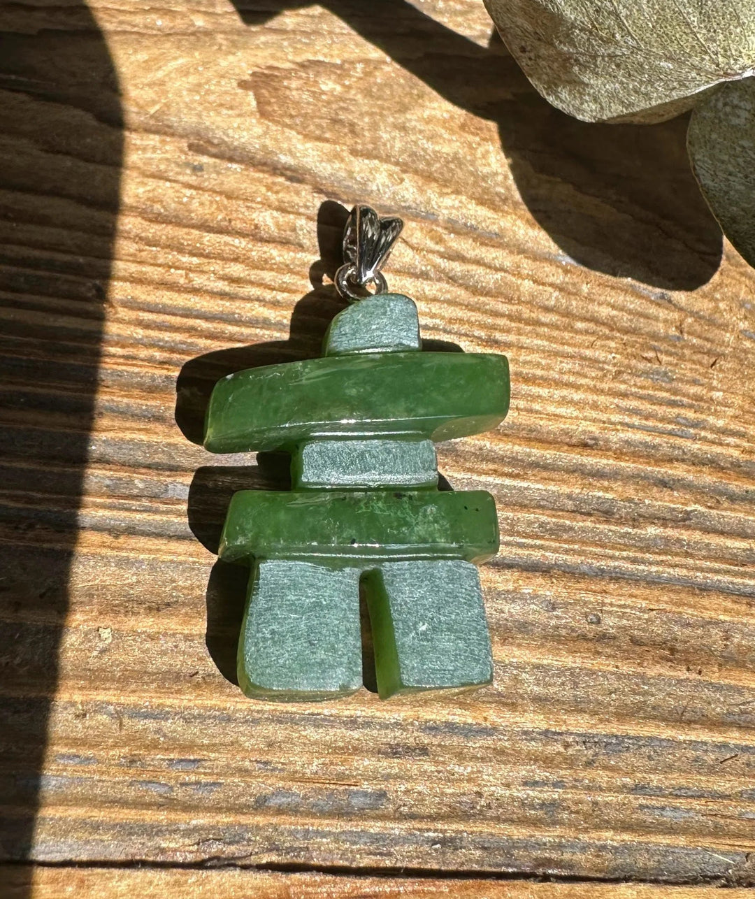 Inukshuk pendant 25mm with stacked green stones and a silver bail resting on a wooden surface.