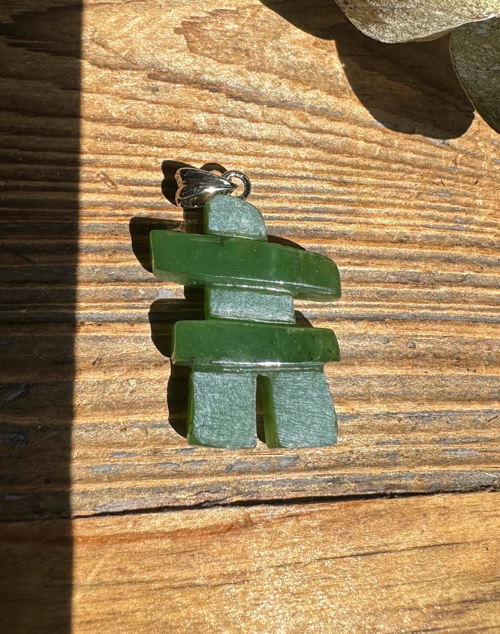 Angled view of Inukshuk pendant with stacked green stones and a silver bail on wood.