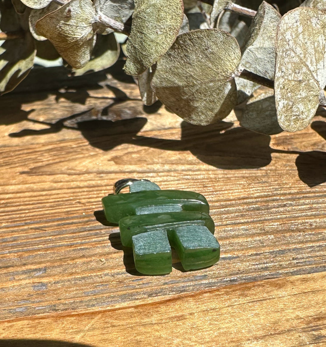 Inukshuk pendant with stacked green stones and silver bail on a wooden surface.