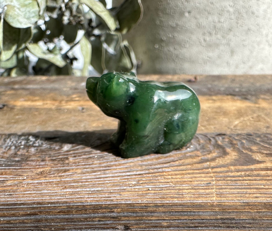 Green jade sitting bear sculpture on a weathered wooden surface with greenery in the background