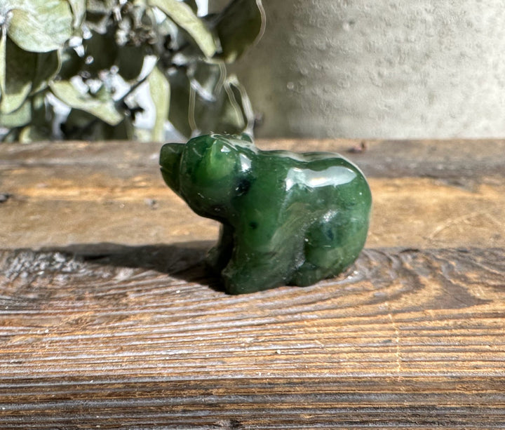 Green jade sitting bear sculpture on a weathered wooden surface with greenery in the background