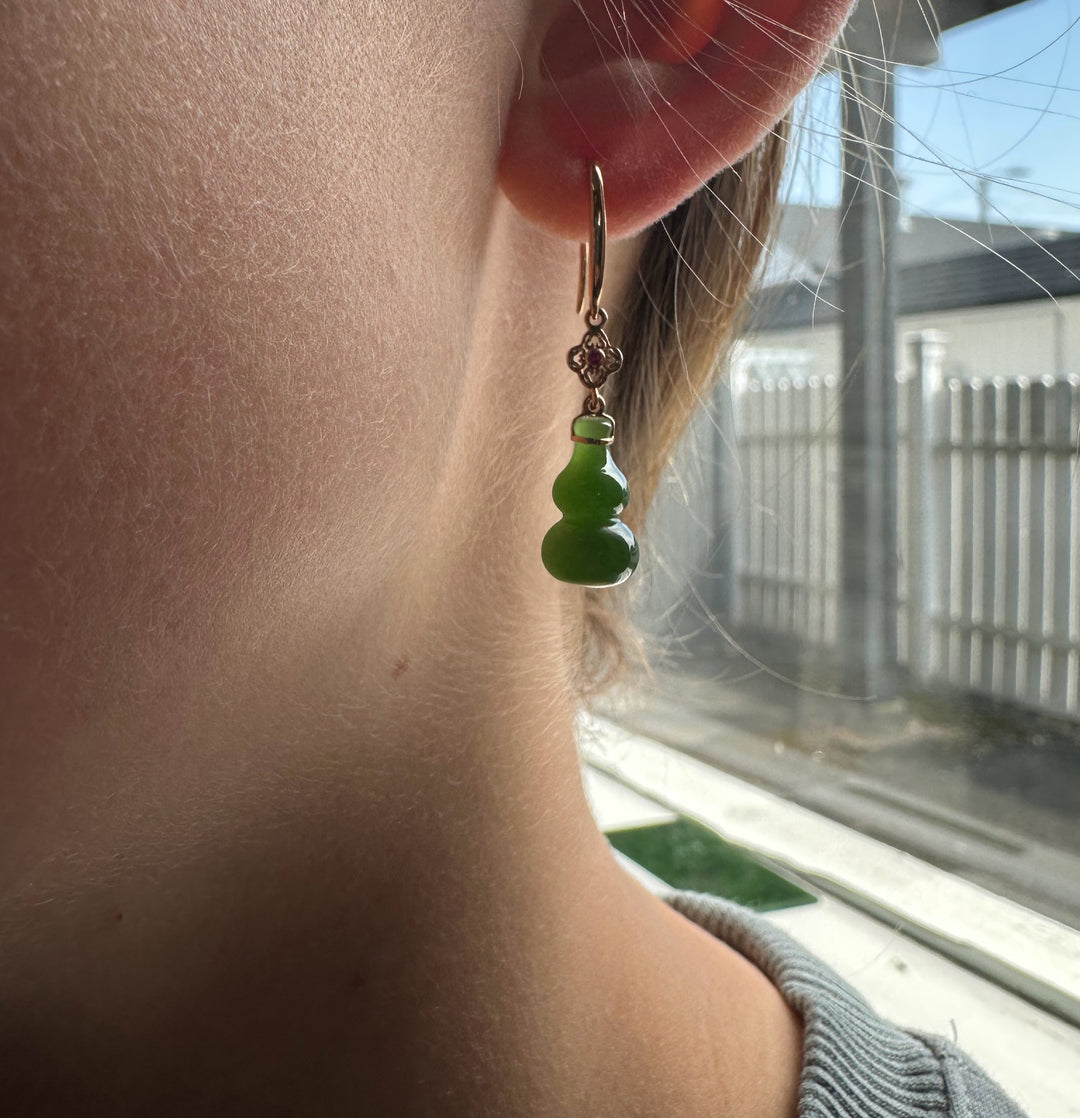 Ear wearing a rose gold hoop earring with a floral connector and a green double gourd pendant.