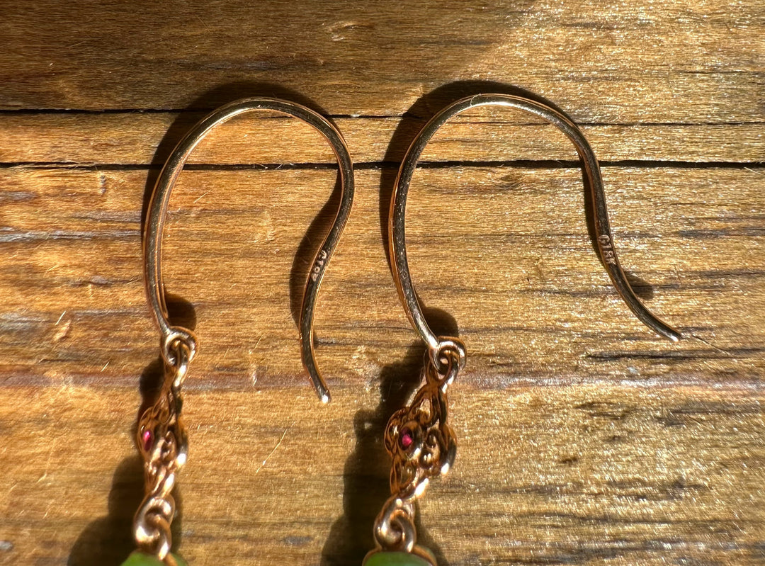 Pair of 18k gold chatoyant gourd earrings with green double drop pendants and pink gemstone accents on a wooden surface.