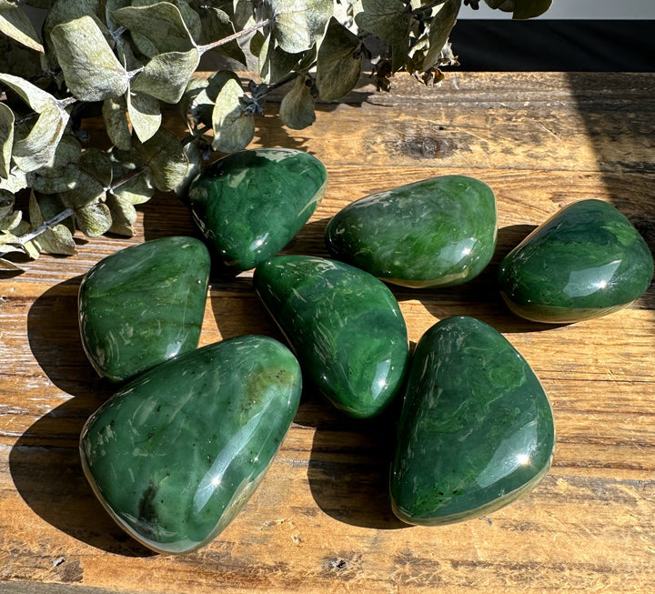 Sunlit green jade stones on a weathered wooden table with dried leaves along the top edge.
