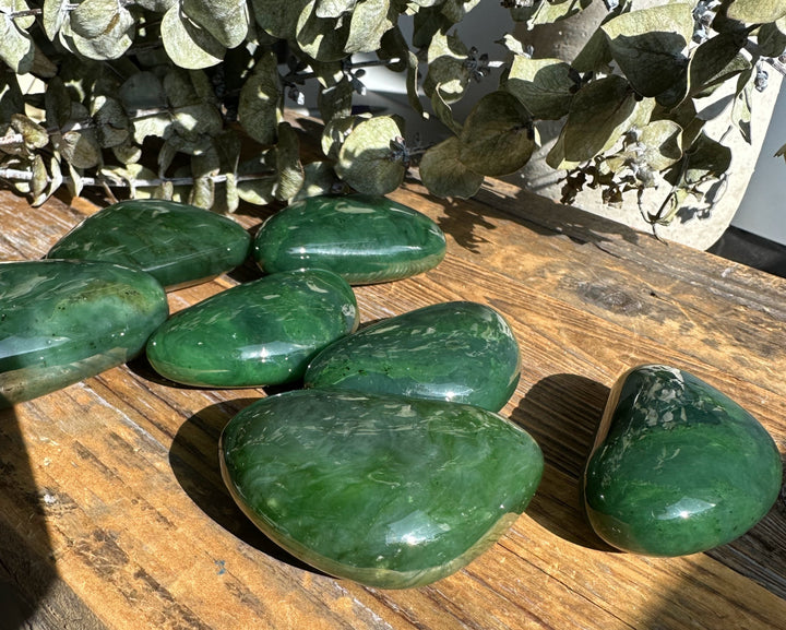 Green jade stones arranged across a rustic wooden tabletop with a cluster of dried leaves in the background.
