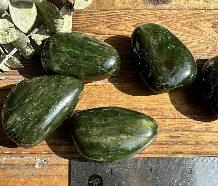 Five sunlit green jade polished specimens on a wooden surface with a ruler for scale