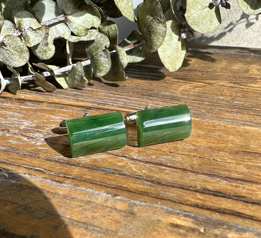 Green jade cufflinks with sterling silver settings resting on a rustic wooden surface.